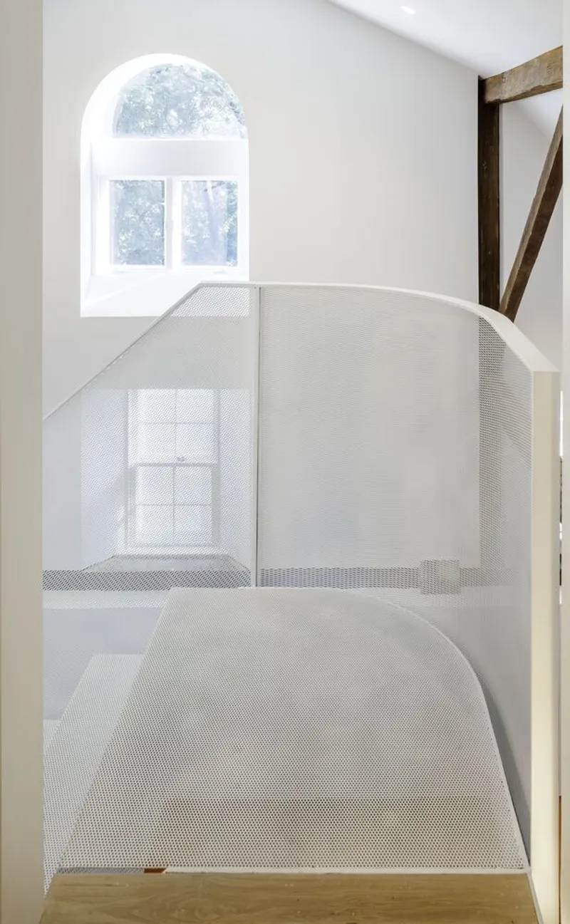 View down onto perforated metal mezzanine floor below arched window with timber bracing visible