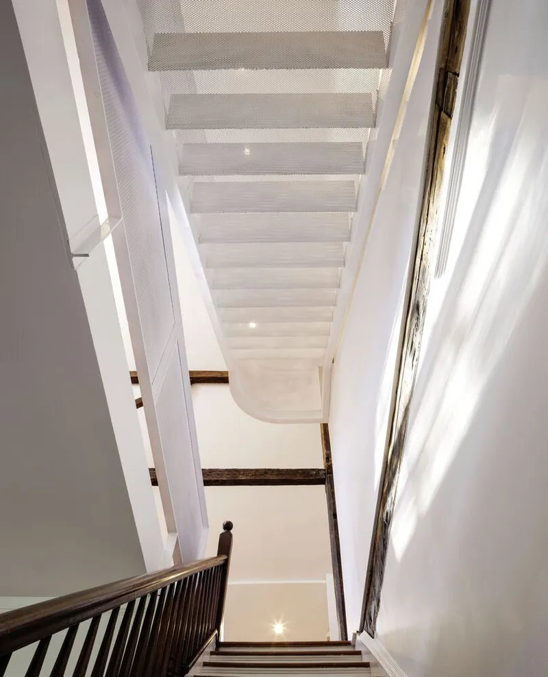 Upward view through stairwell with perforated metal landing, exposed timber beams, and skylight above
