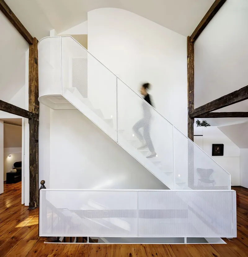 Perforated white metal staircase with a figure ascending past exposed timber columns