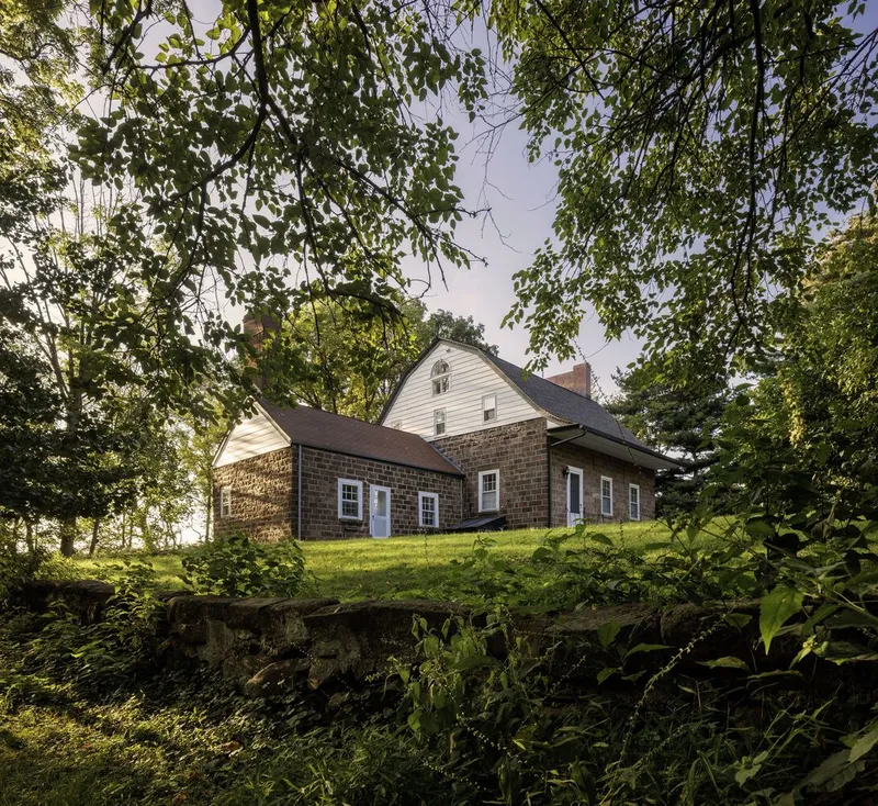 Weathered shingle facades with gabled roof forms on a grassy slope beneath deciduous trees