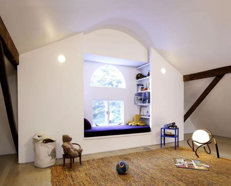 Arched window alcove with purple cushioned seat, built-in shelving, exposed timber beams, and scattered toys on the floor