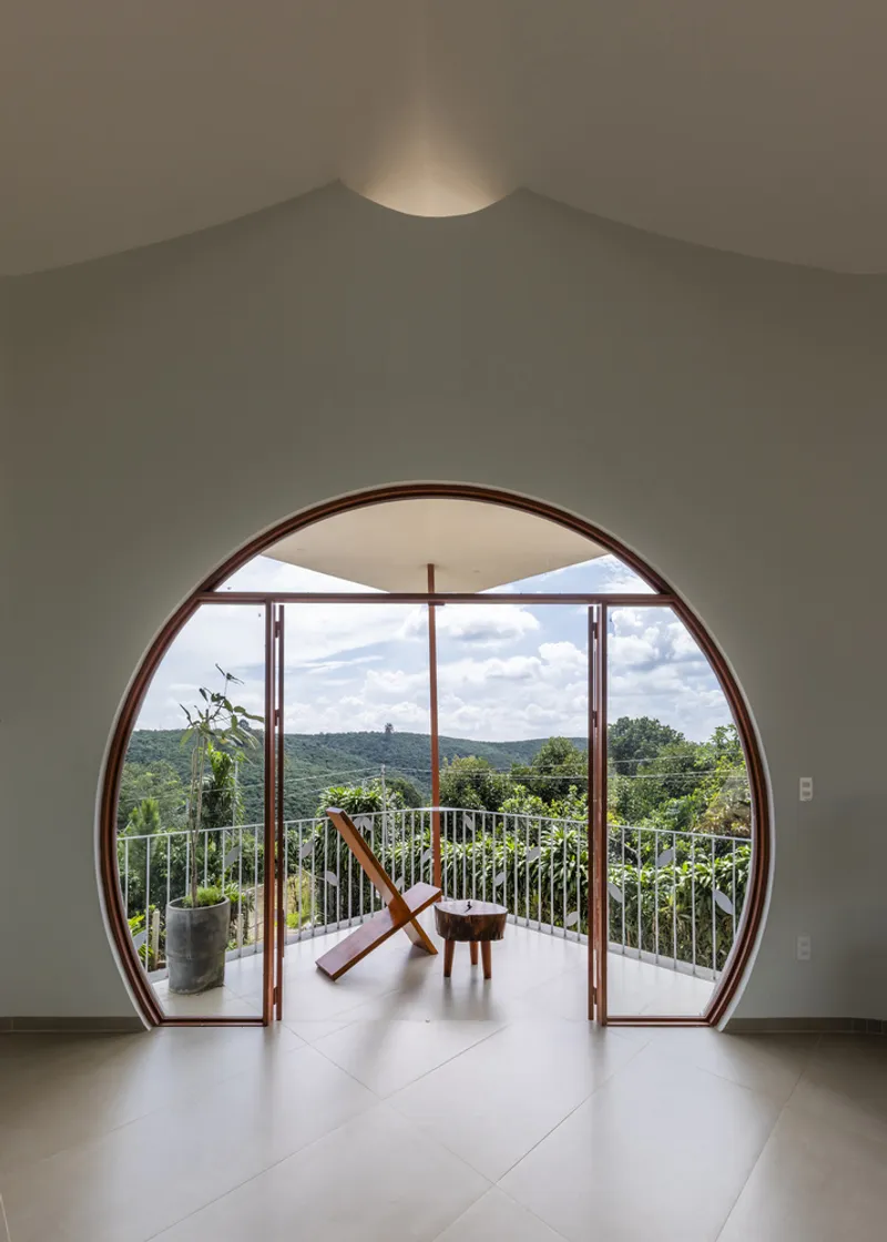 Circular door opening with timber frame leading to balcony with folding chair and view of forested hillside