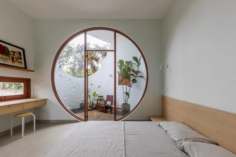Bedroom with circular timber-framed door opening to a private courtyard with armchair and plants