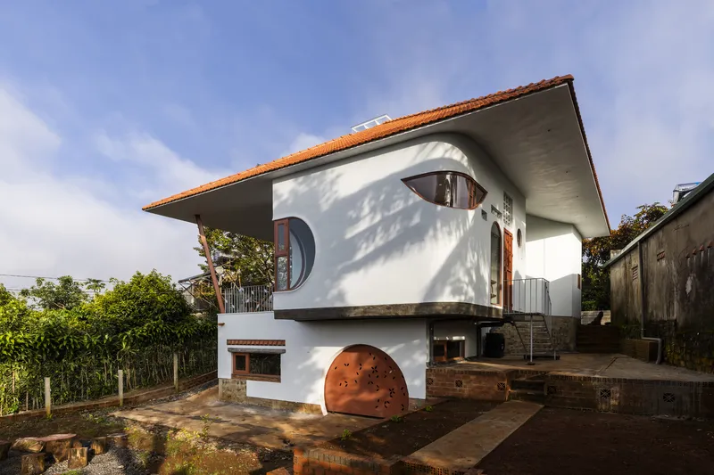 Side elevation showing the overhanging terracotta roof and circular windows casting shadows on white stucco walls