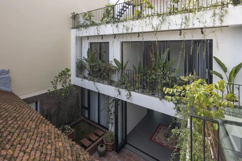 From upper level: planted balconies, white walls, terracotta-tiled rooftop of the ancestral hall visible below at left, courtyard floor