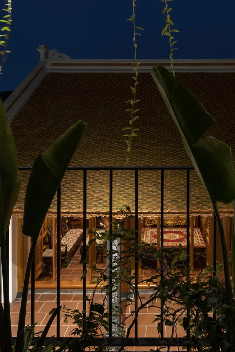 Night: ancestral hall with terracotta tiled roof glowing warm, banana plants in the foreground