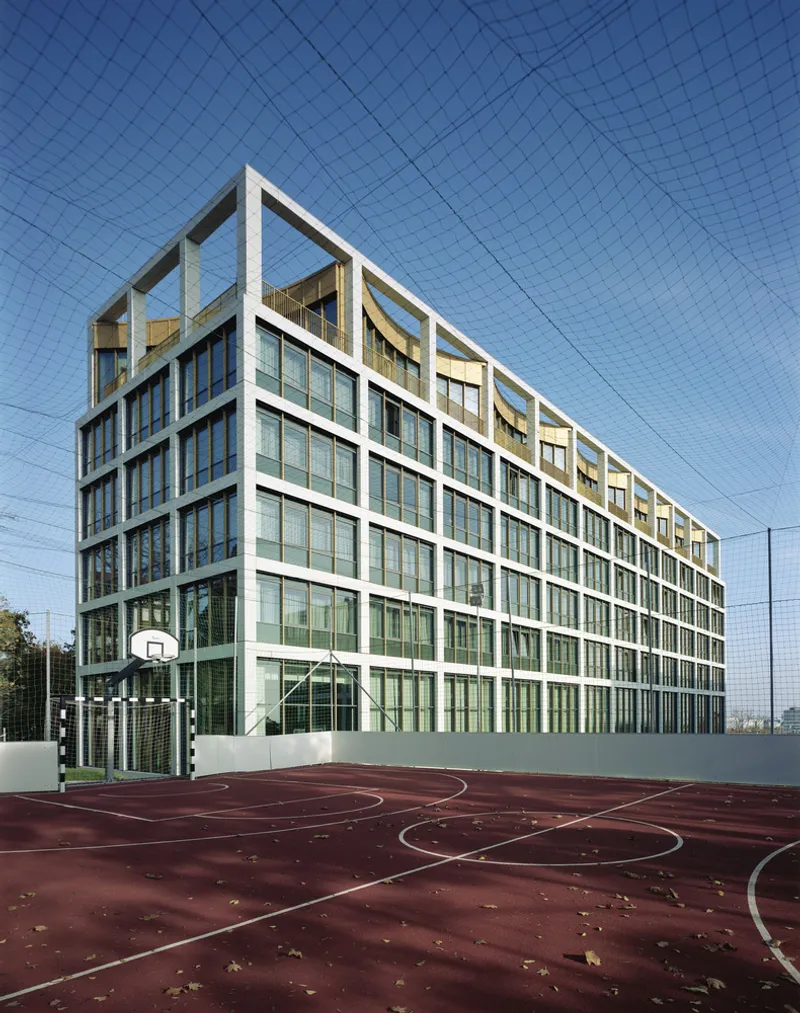 Glass and white concrete frame facade viewed across a maroon sports court with basketball hoops