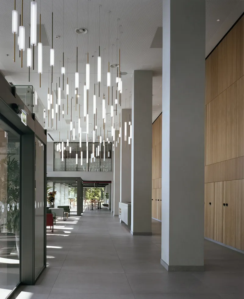 Double-height lobby with suspended tubular pendant lights and wood-clad walls flanking gray columns
