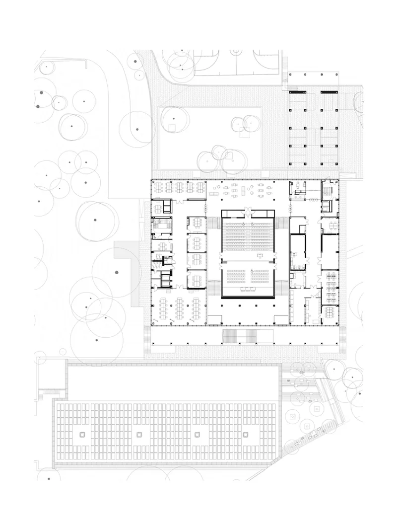 Site plan drawing showing an L-shaped building with courtyards, parking area, and surrounding landscaped grounds with circular trees