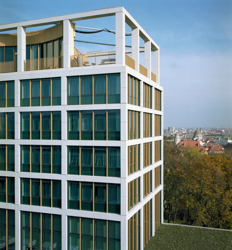 Corner view of the white framed facade with recessed balconies and golden panels overlooking autumn foliage