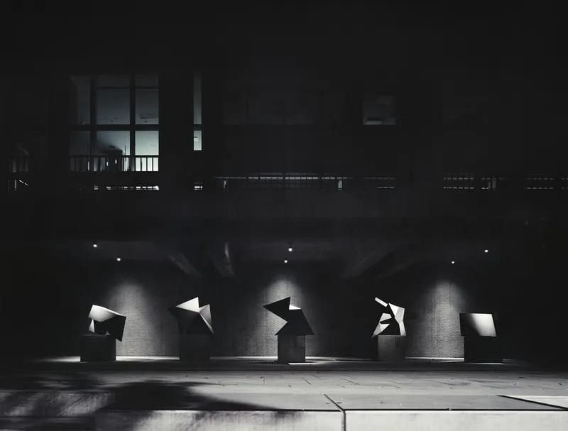 Concrete ceiling with exposed beams and angular cutout windows illuminated by spotlights at night