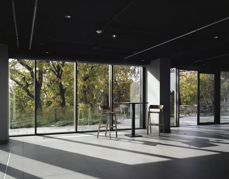 Interior gallery space with floor-to-ceiling glass walls framing views of trees in sunlight