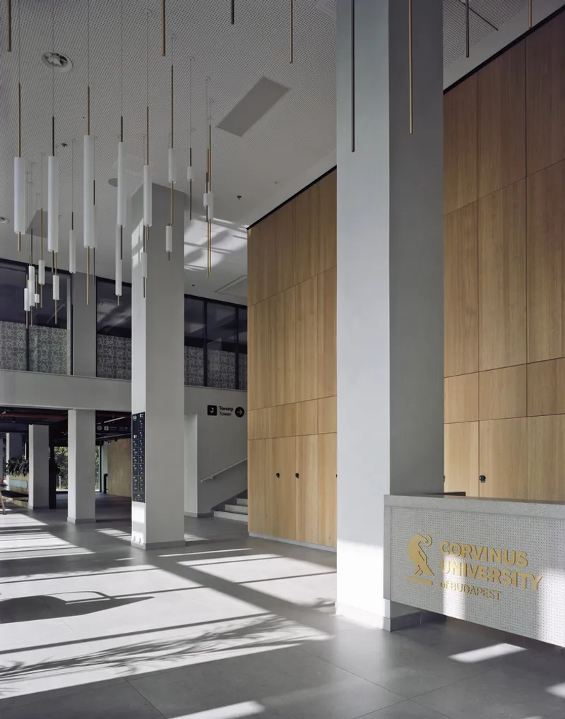 Double-height lobby with white columns, suspended tubular pendant lights, and timber wall panels in morning sunlight
