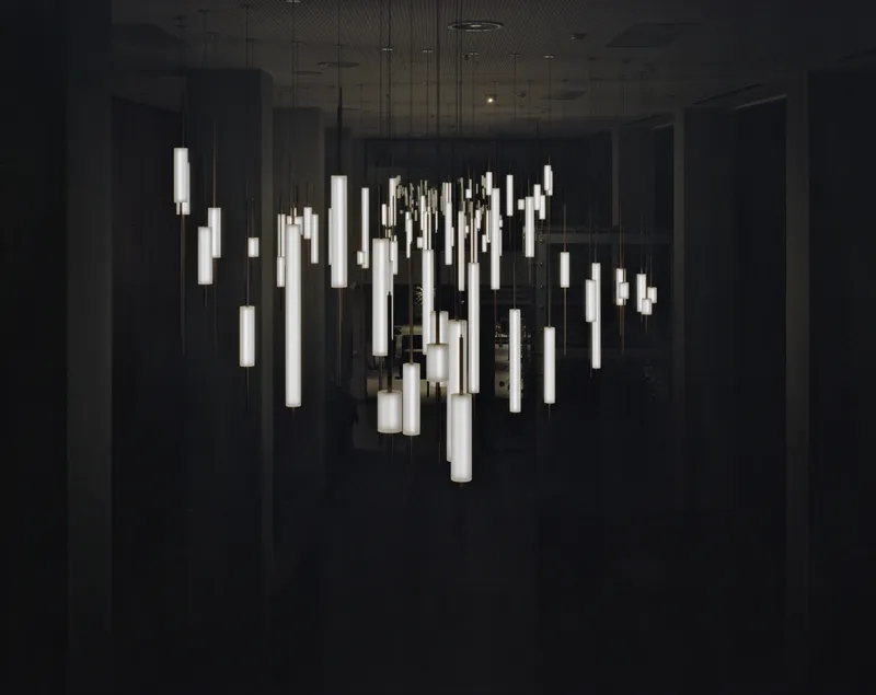 Cluster of cylindrical pendant lights suspended at varying heights against a dark wall