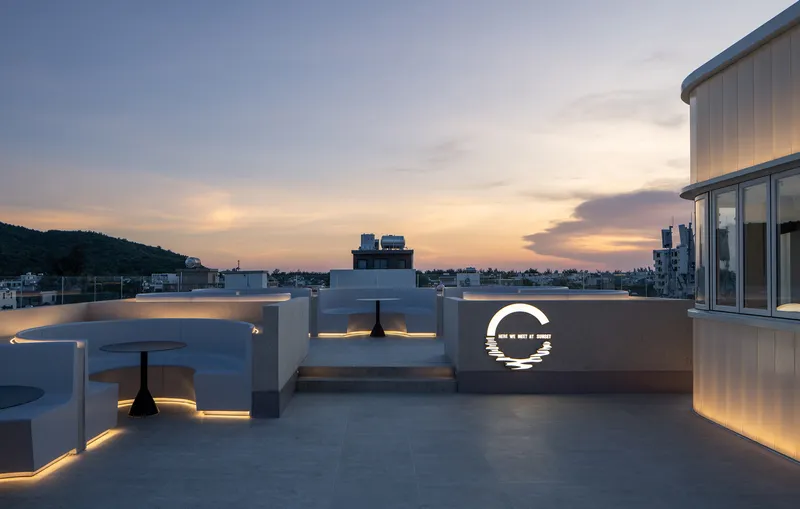Rooftop terrace with curved white seating walls and illuminated circular logo panel at sunset