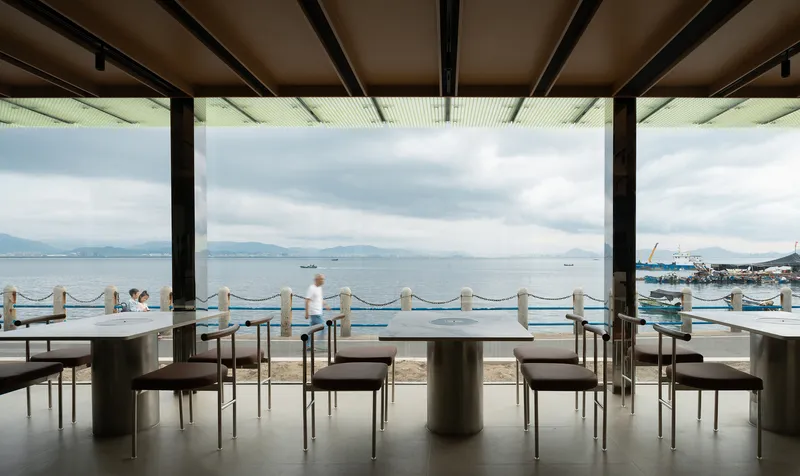 Covered dining area with timber tables and rope railing overlooking the harbor and distant mountains