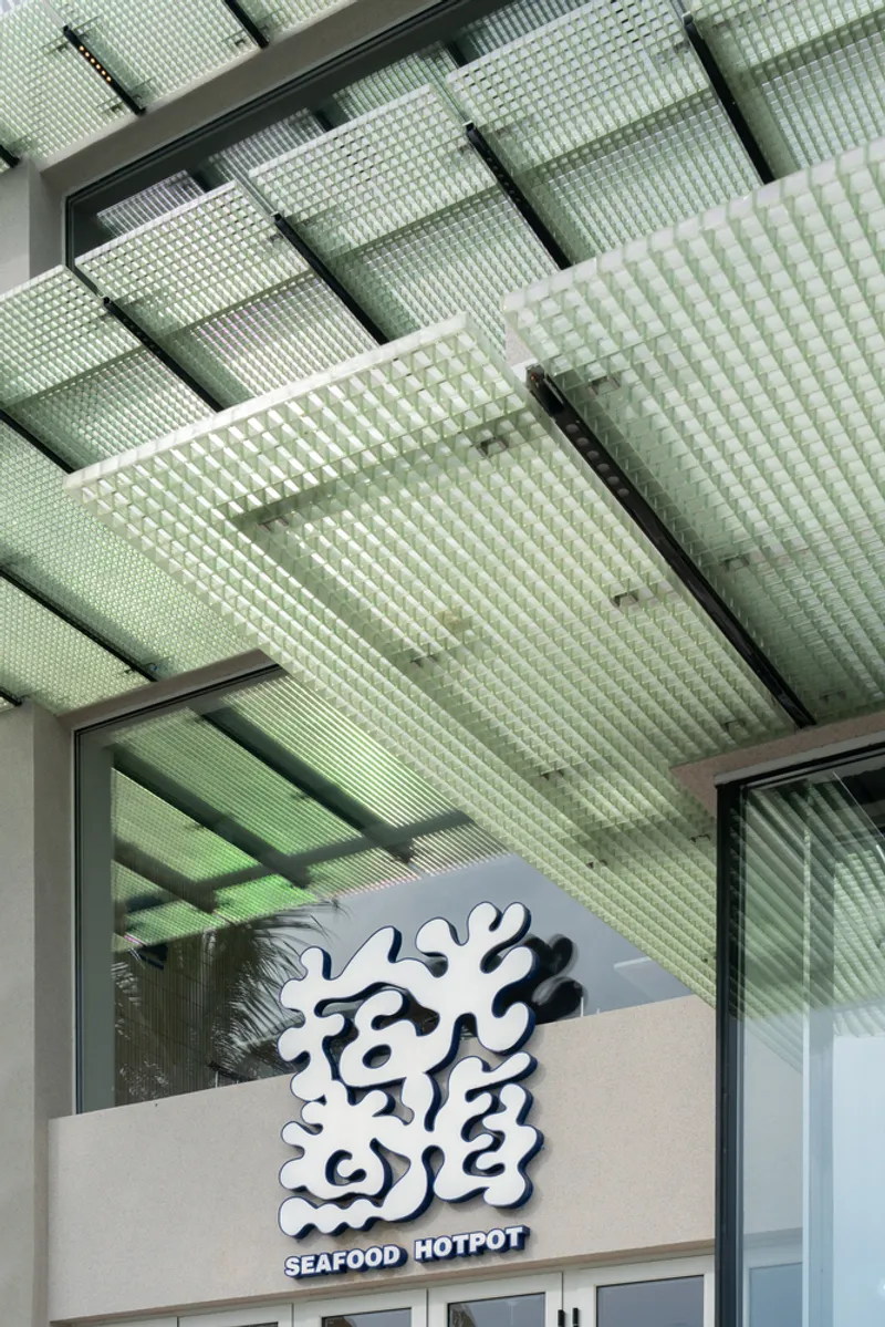 Entry detail showing translucent perforated green canopy panels above signage and glazed storefront