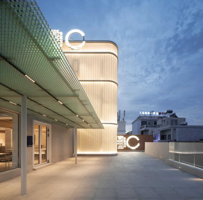 Rooftop terrace with illuminated cylindrical tower clad in ribbed panels and perforated green canopy at twilight
