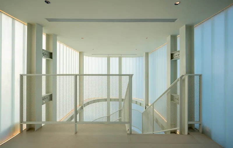 Interior stairwell with metal mesh guardrail and floor-to-ceiling translucent curtains filtering daylight