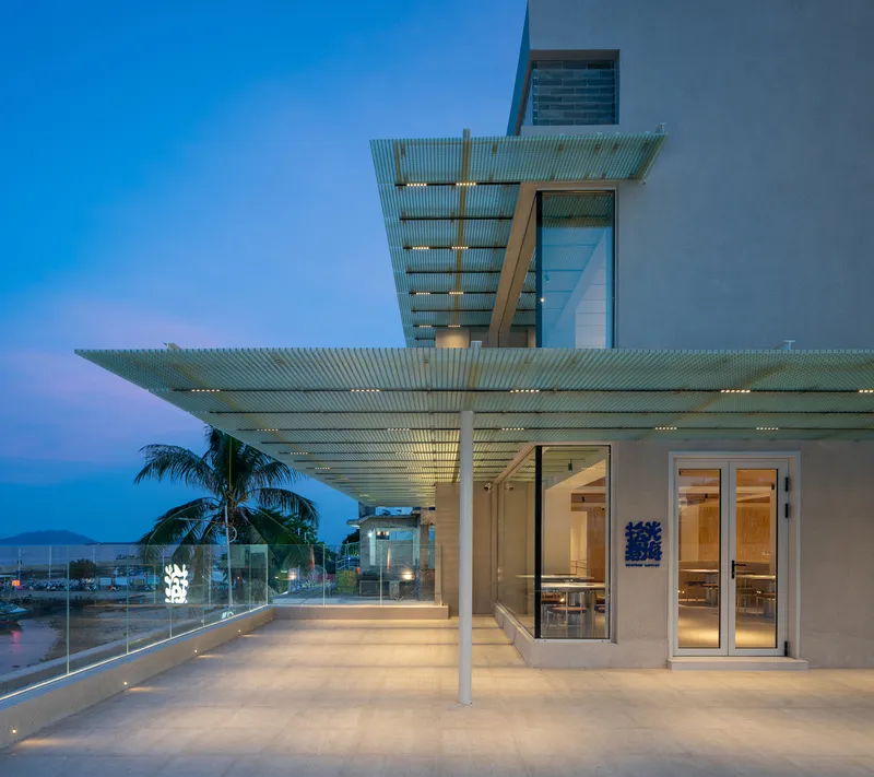 Covered terrace with perforated metal canopy and glass balustrade at dusk under a blue sky