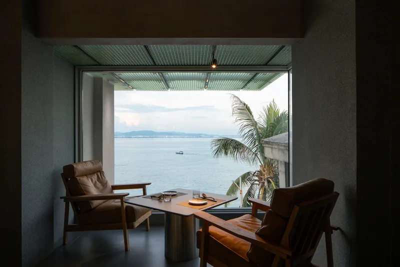 Framed ocean view through a corrugated metal ceiling with leather lounge chairs and palm fronds outside