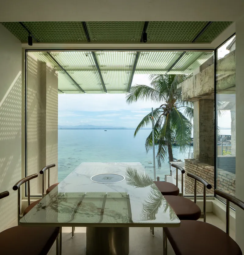 Dining table beneath a perforated ceiling with reflected light patterns and an infinity pool beyond palm trees