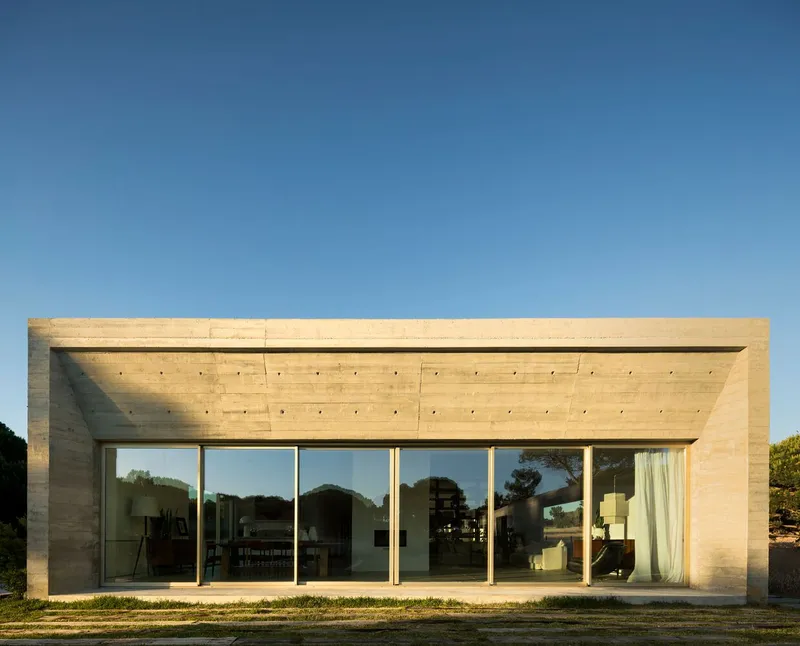 Glazed facade with floor-to-ceiling windows beneath a board-formed concrete overhang at dusk