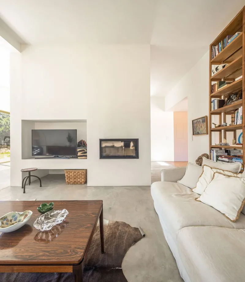 Living room with white plaster fireplace wall, timber shelving, and polished concrete floor in daylight
