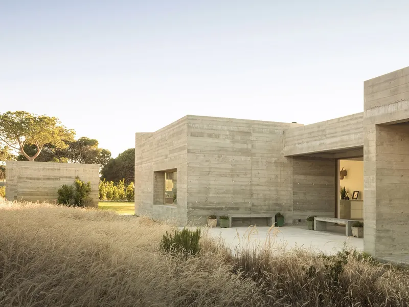 Board-formed concrete volumes surrounding a terrace in dry golden grassland under late afternoon light