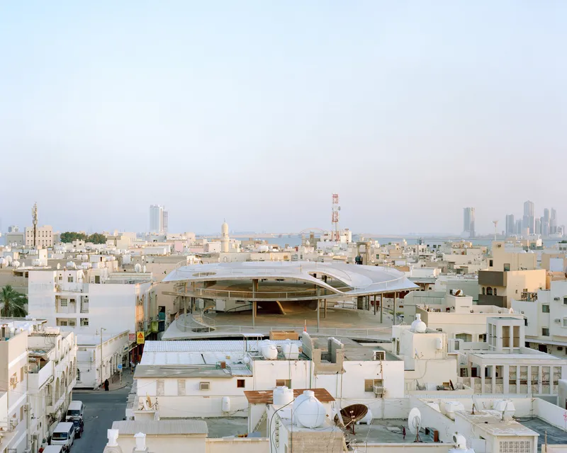 Curved roof canopy rising above the low-rise rooftops of the surrounding neighborhood at dusk