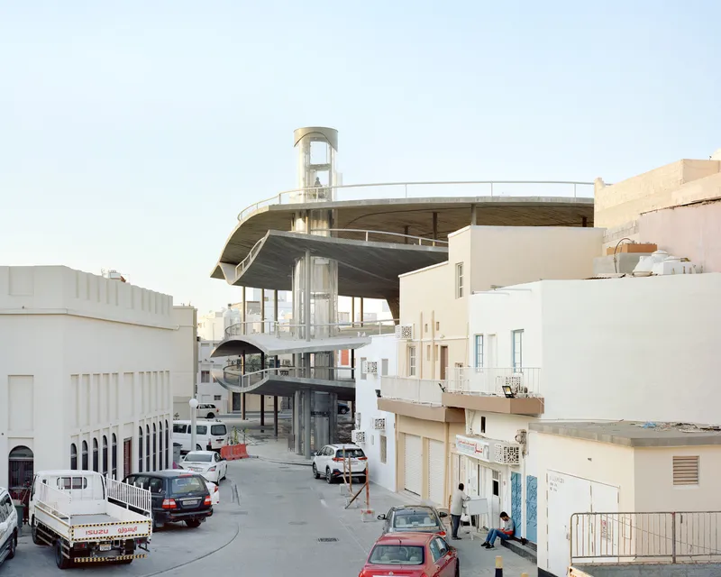 Layered concrete roof decks with exposed columns and spiral stair tower above a street with parked cars