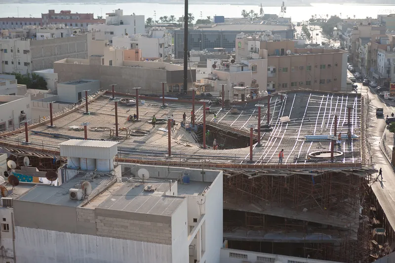 Construction site showing steel rebar formwork for a curved roof structure in midday sunlight