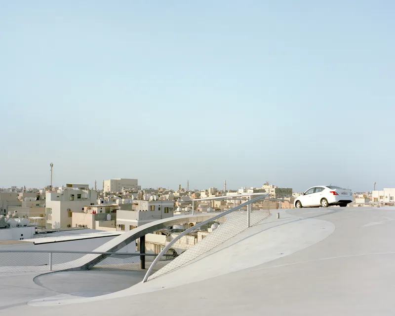 Rooftop view of the curving ramp and parked car against a low-rise residential skyline