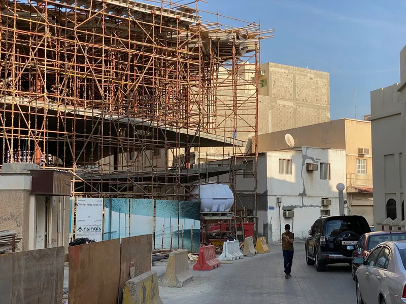 Street view of timber scaffolding surrounding the concrete structure under construction with a pedestrian passing