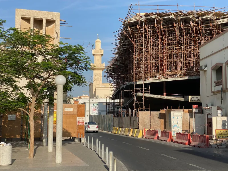 Construction site with timber formwork beside a minaret and young street trees in afternoon light