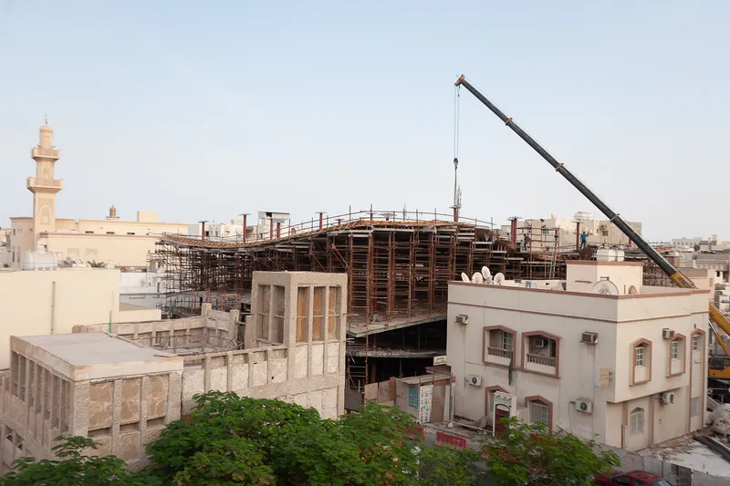 Crane hovering over the curved timber formwork rising above surrounding residential rooftops at dusk