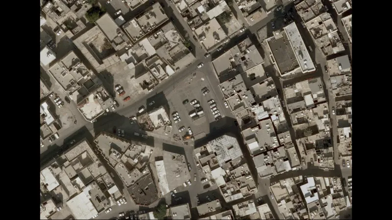Aerial view of a dense urban block with flat rooftops, parked cars and narrow streets