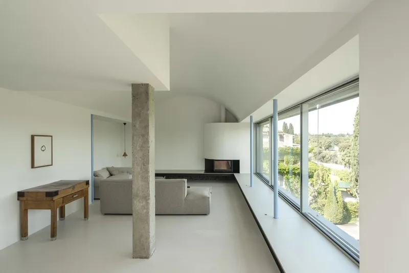 Open-plan living space with exposed concrete column and continuous horizontal windows overlooking green landscape