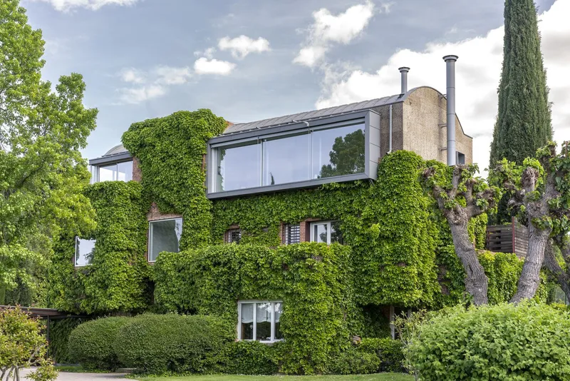 Ivy-clad facade with ribbon window and twin metal chimneys under a partly cloudy sky