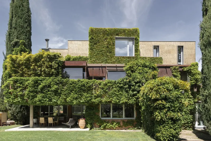 Garden facade showing three levels of vegetation-covered volumes with terracotta chimneys and cypress trees