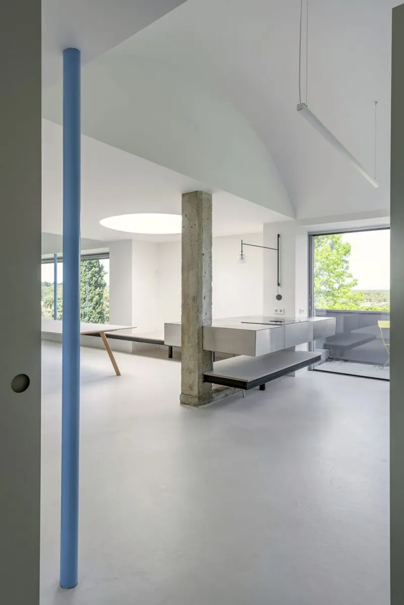 Living space with blue steel columns, concrete pillar, and suspended linear lighting fixture overhead