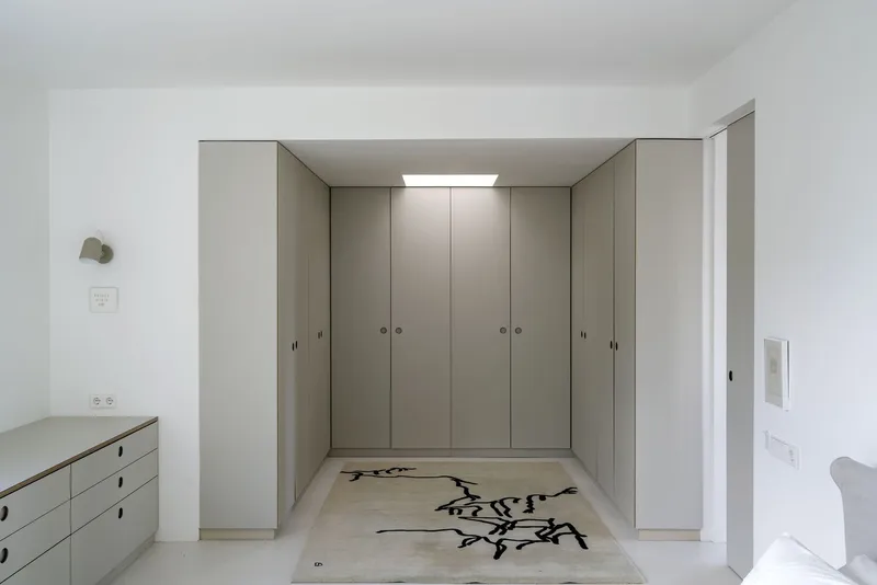 Bedroom with floor-to-ceiling storage cabinets and rug featuring calligraphic motif under skylight