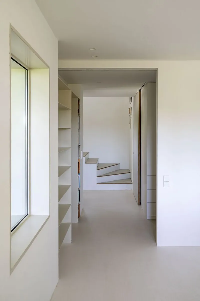 Hallway with built-in shelving leading to a staircase with timber handrail and angled steps