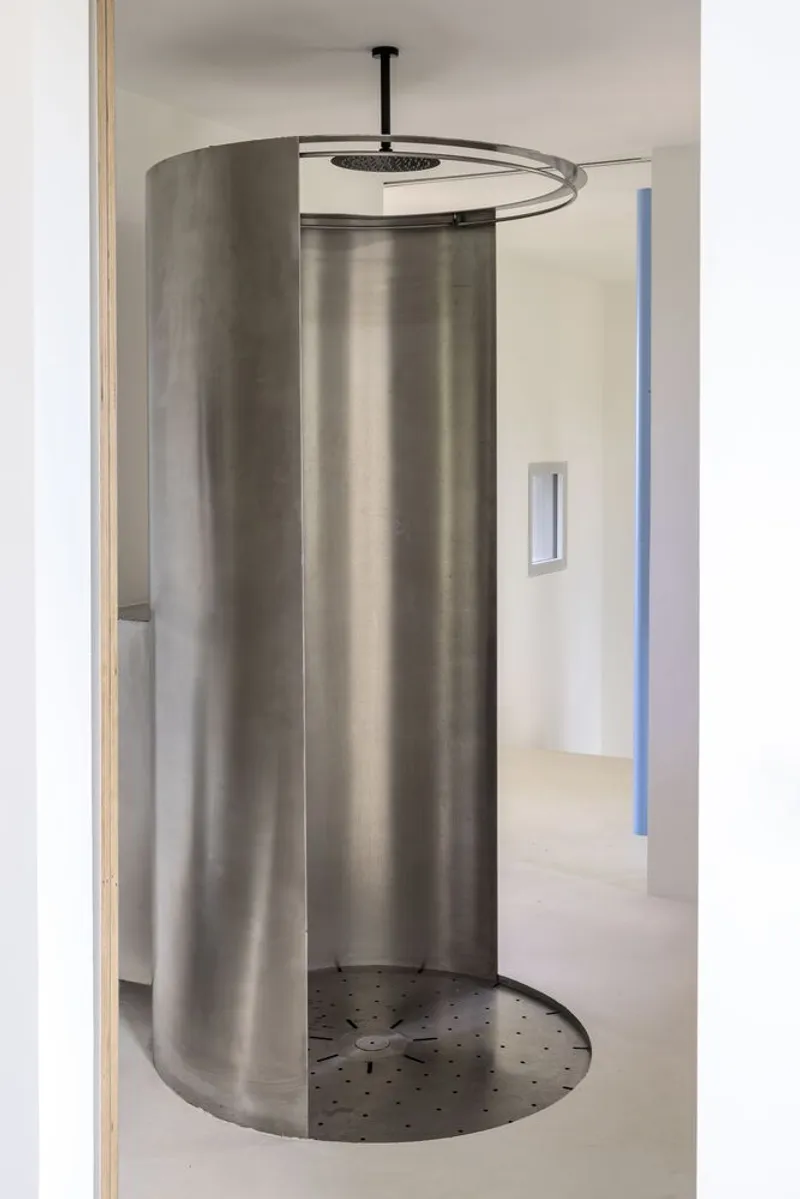 Close view of the curved metal shower screen with overhead rain showerhead and drainage holes