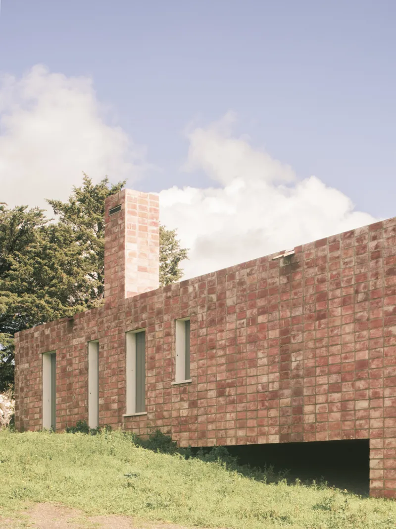 Red brick facade with vertical slit windows and exposed chimney stack on a sloping lawn