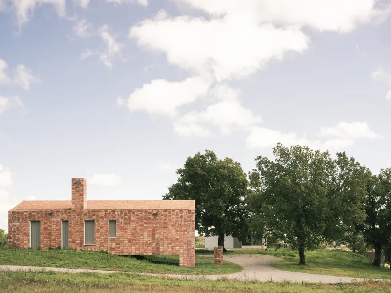 Red brick volume with narrow vertical windows set on a grassy hillside among mature trees