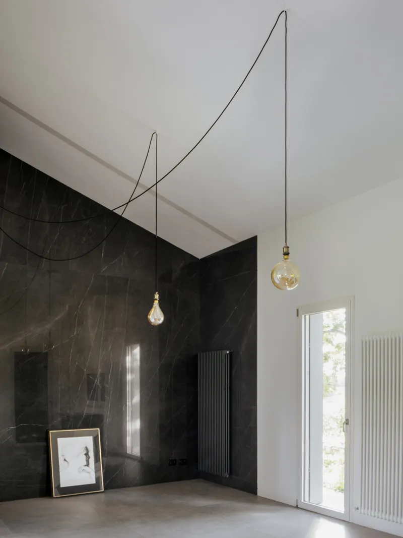 Black marble wall with exposed cable pendant lights and tall window casting natural light across concrete floor
