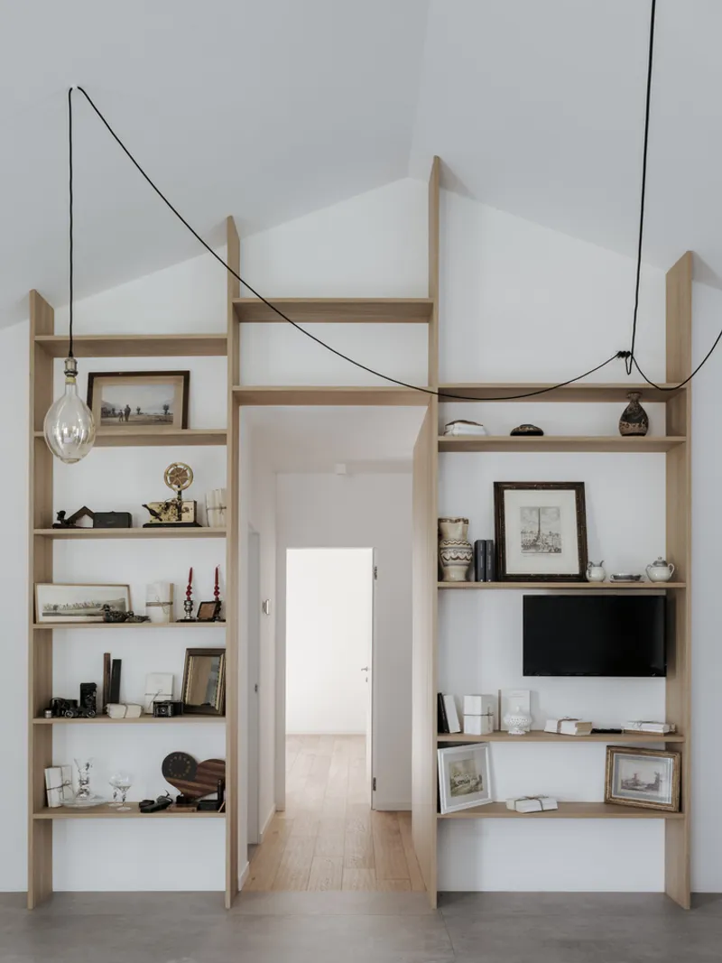 Built-in shelving units flanking a doorway with exposed cable pendant lights and gabled ceiling forms