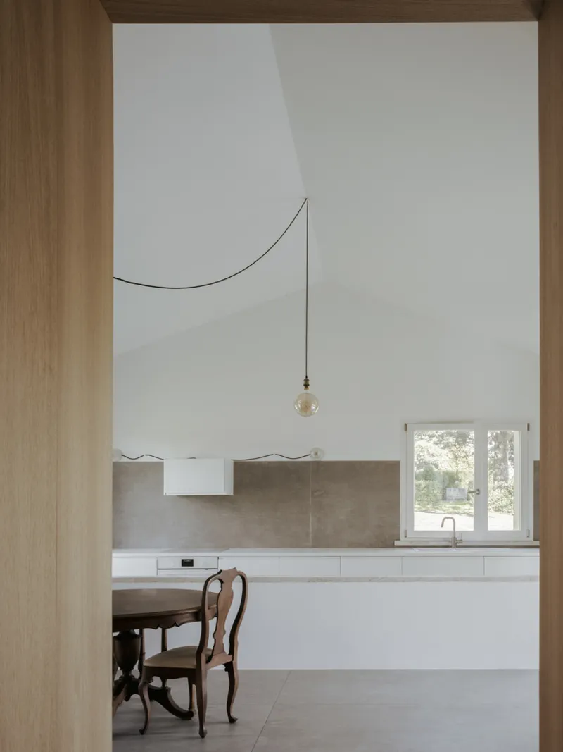 Kitchen framed by timber opening showing white cabinetry with stone backsplash and pendant light