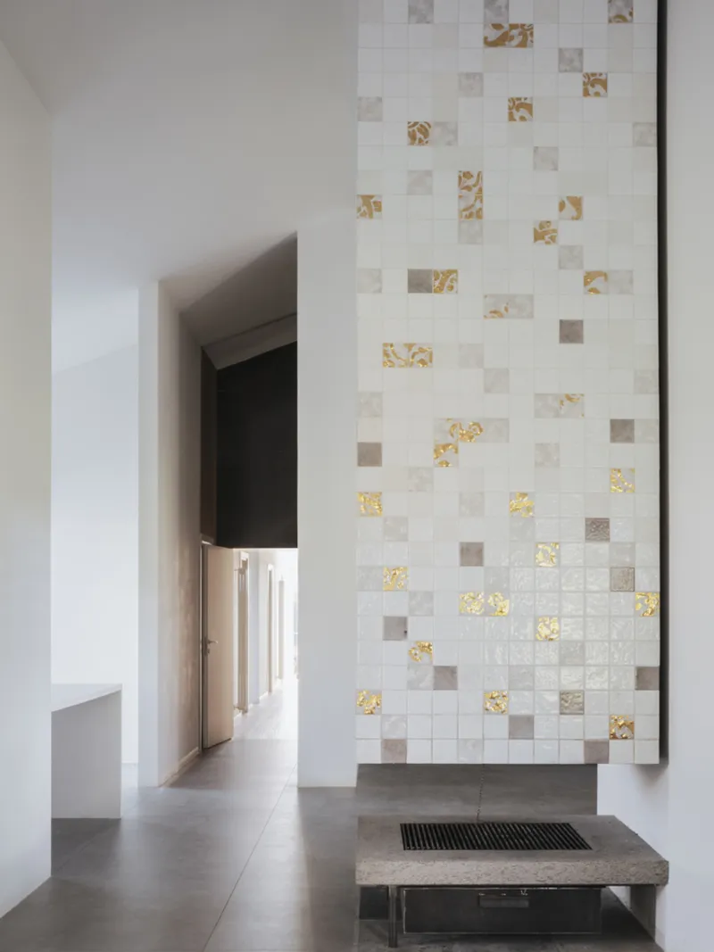 Tiled mosaic wall with gold-leaf accents above a concrete bench in a bright corridor